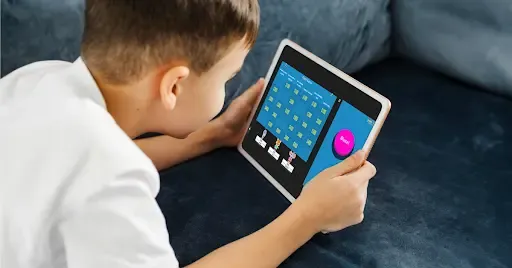 Child playing an educational Jeopardy-style game on a tablet while lying on a couch.