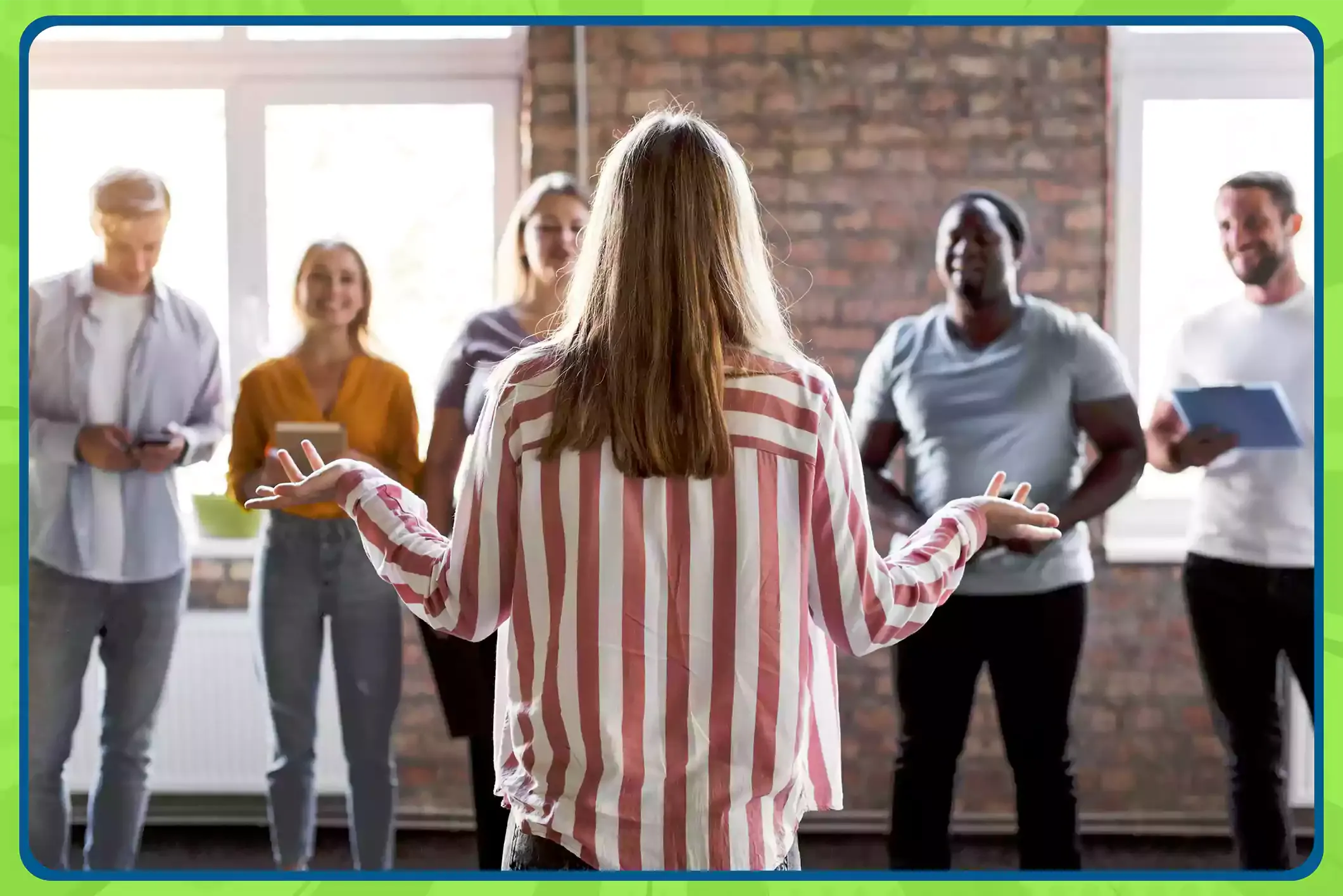 A woman stands in front of coworkers in an office, playing a game of charades with everyone smiling and guessing.