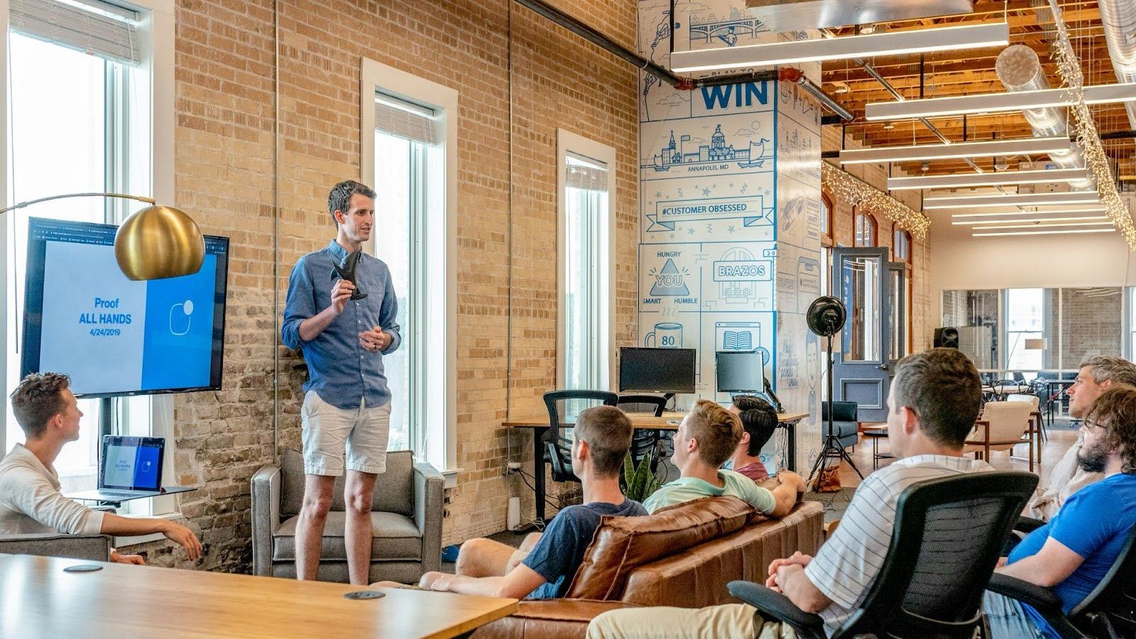 Team meeting discussing an EdTech tool, with a presenter by a screen and attendees seated in a modern office space