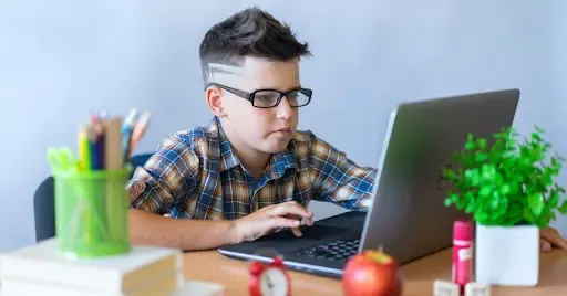 Child focused on working at a laptop in a study area.