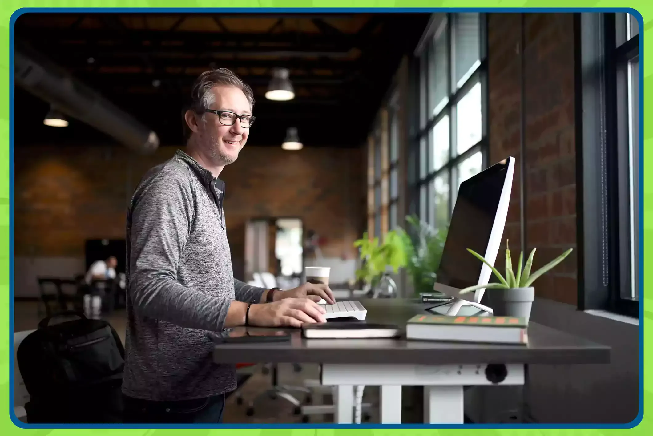 Man smiling at a standing desk in an office, playing office trivia on his computer.